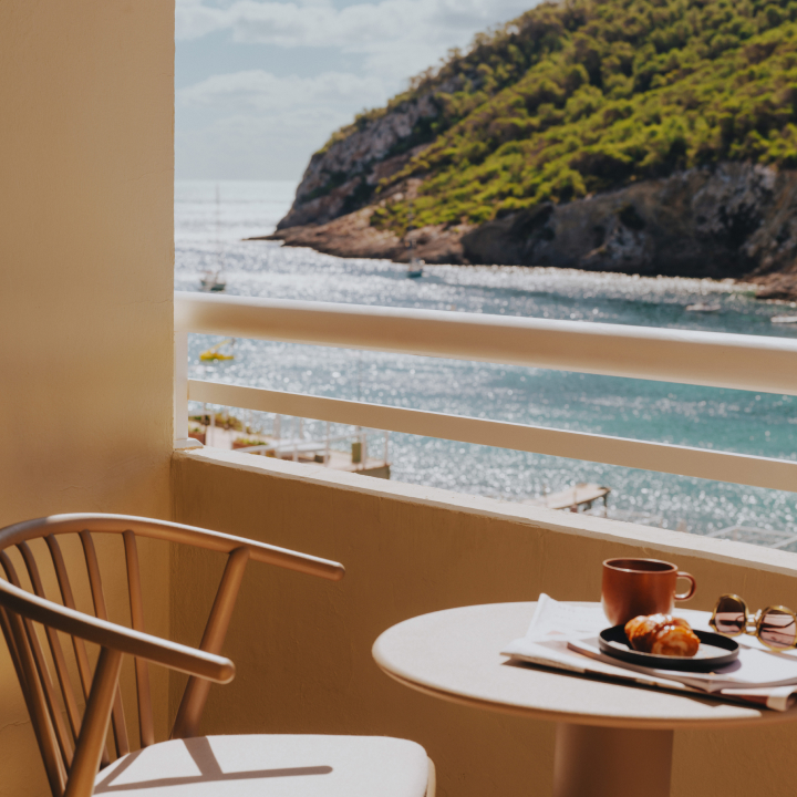 A chair on a balcony overlooking the sea with mountains in the distance