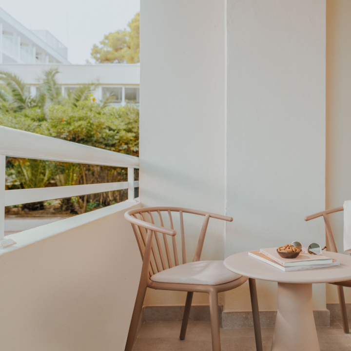 A table and two chairs on a balcony with trees in the distance