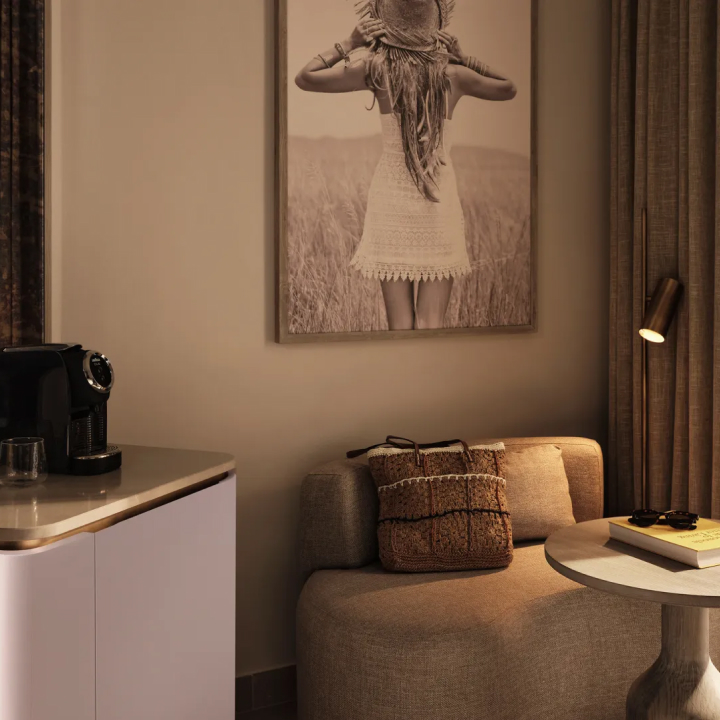 A comfy seat with cushion next to a side table, below artwork