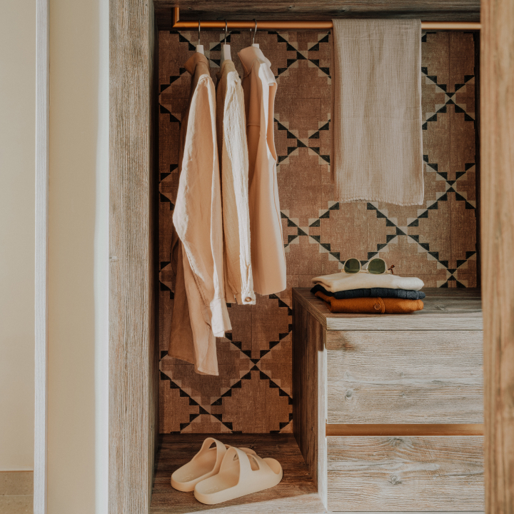 Three shirts hanging in a wardrobe.with folded shirts sitting on top of drawers