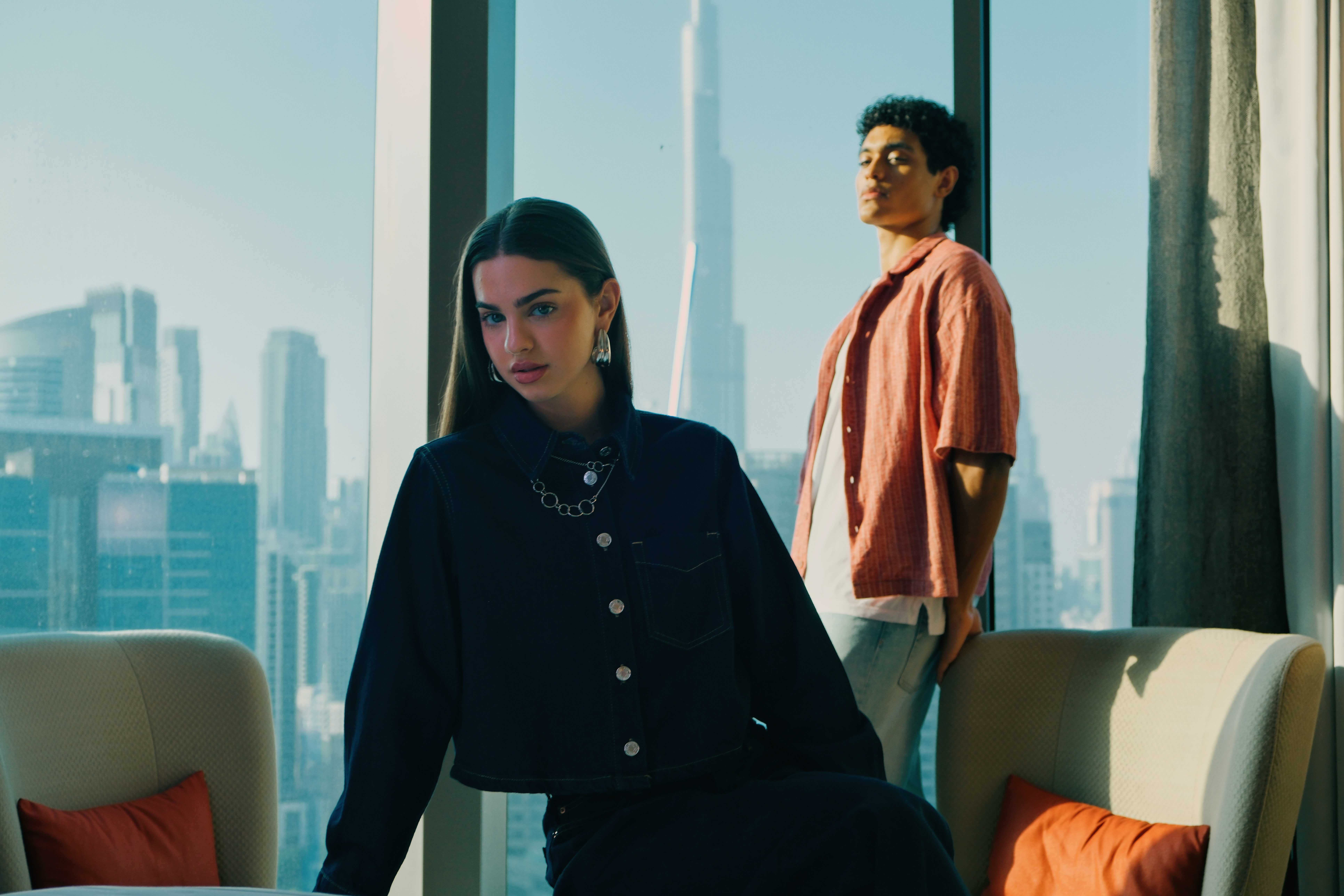 A guy and a lady in a room with a view of the Burj Khalifa visible through the window.