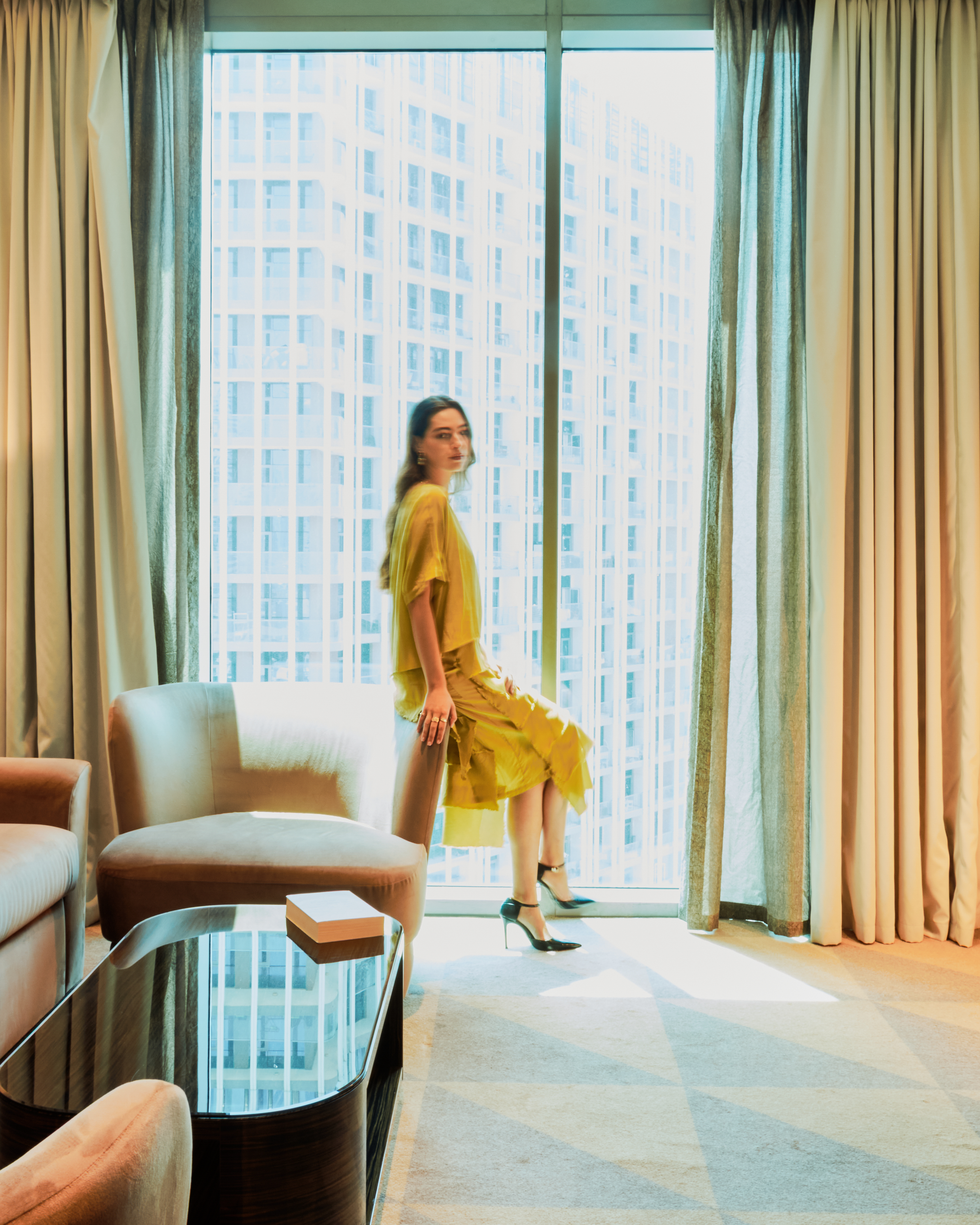 A woman sitting next to a window in a hotel room with soft natural light illuminating the space.