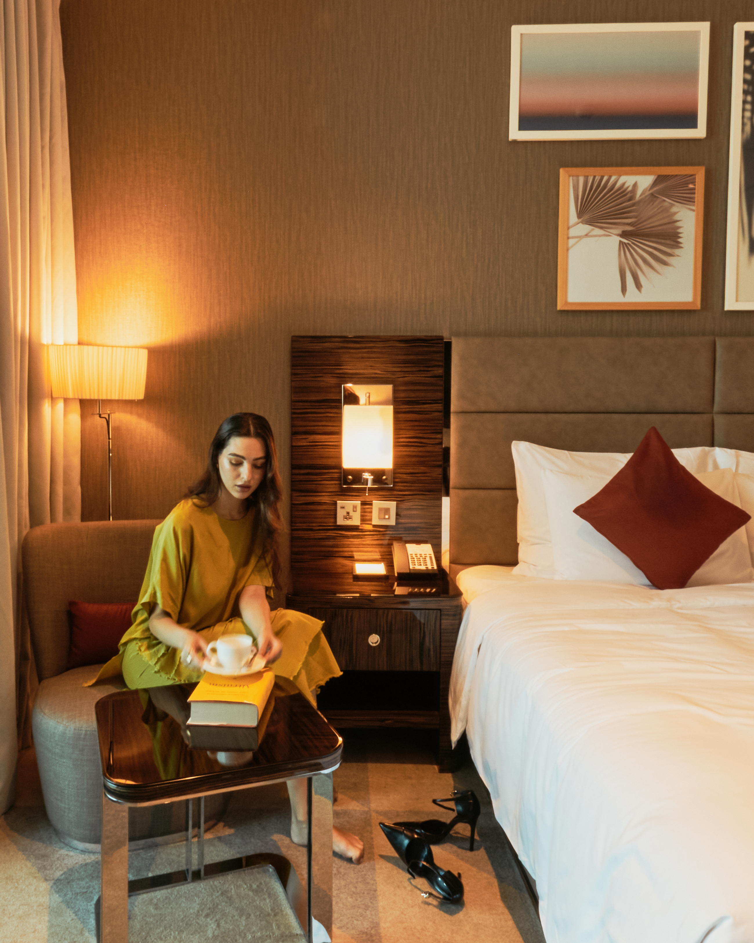 A woman sitting on an armchair in a hotel room, holding a cup of drink