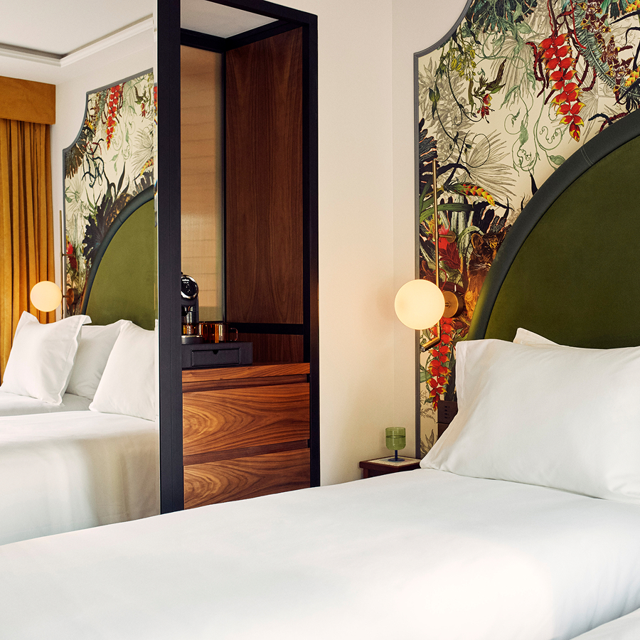 Bed with floral wallpaper behind, infront of an open wardrobe door