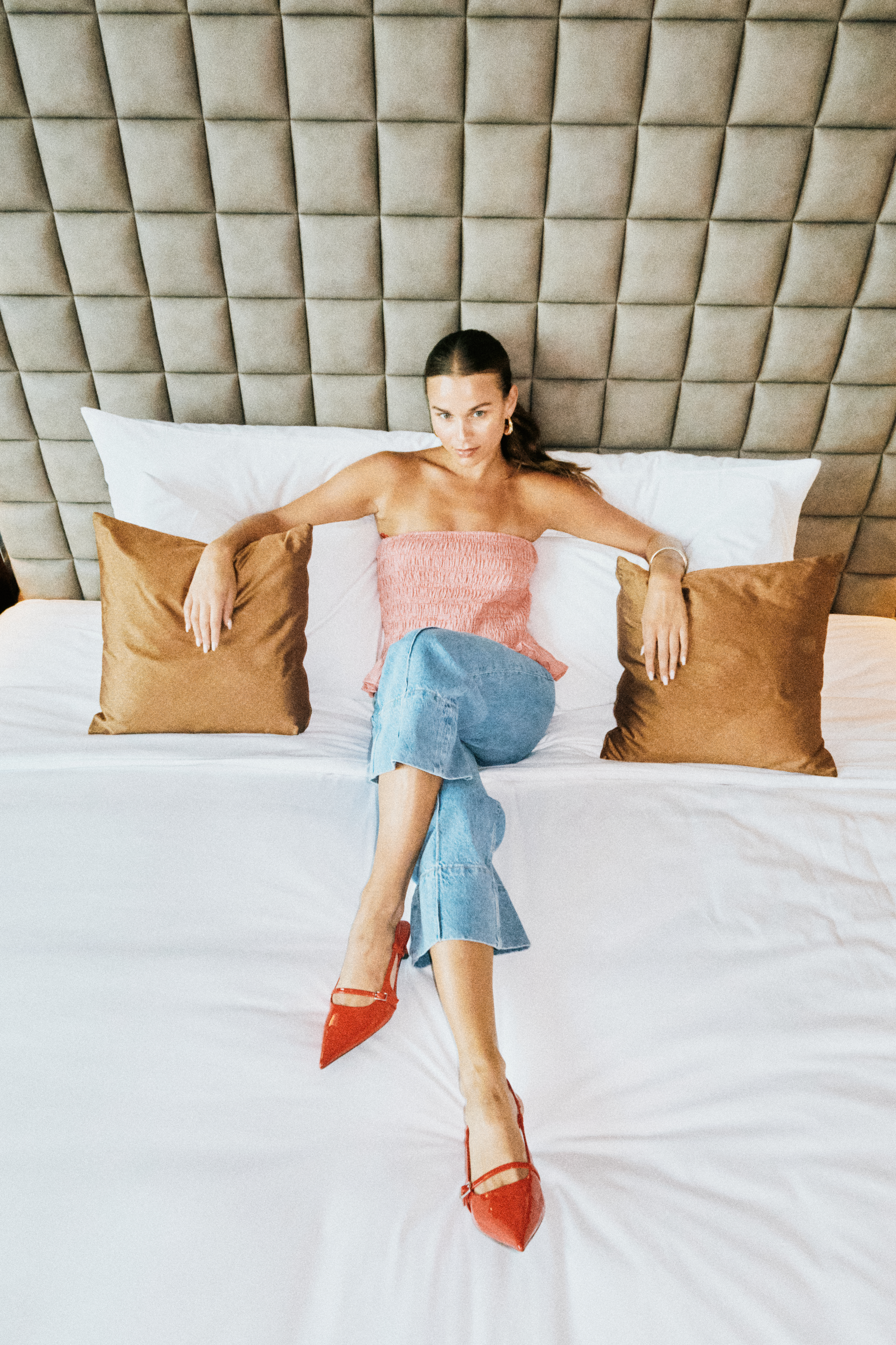A woman sitting in bed, surrounded by pillows and cushions