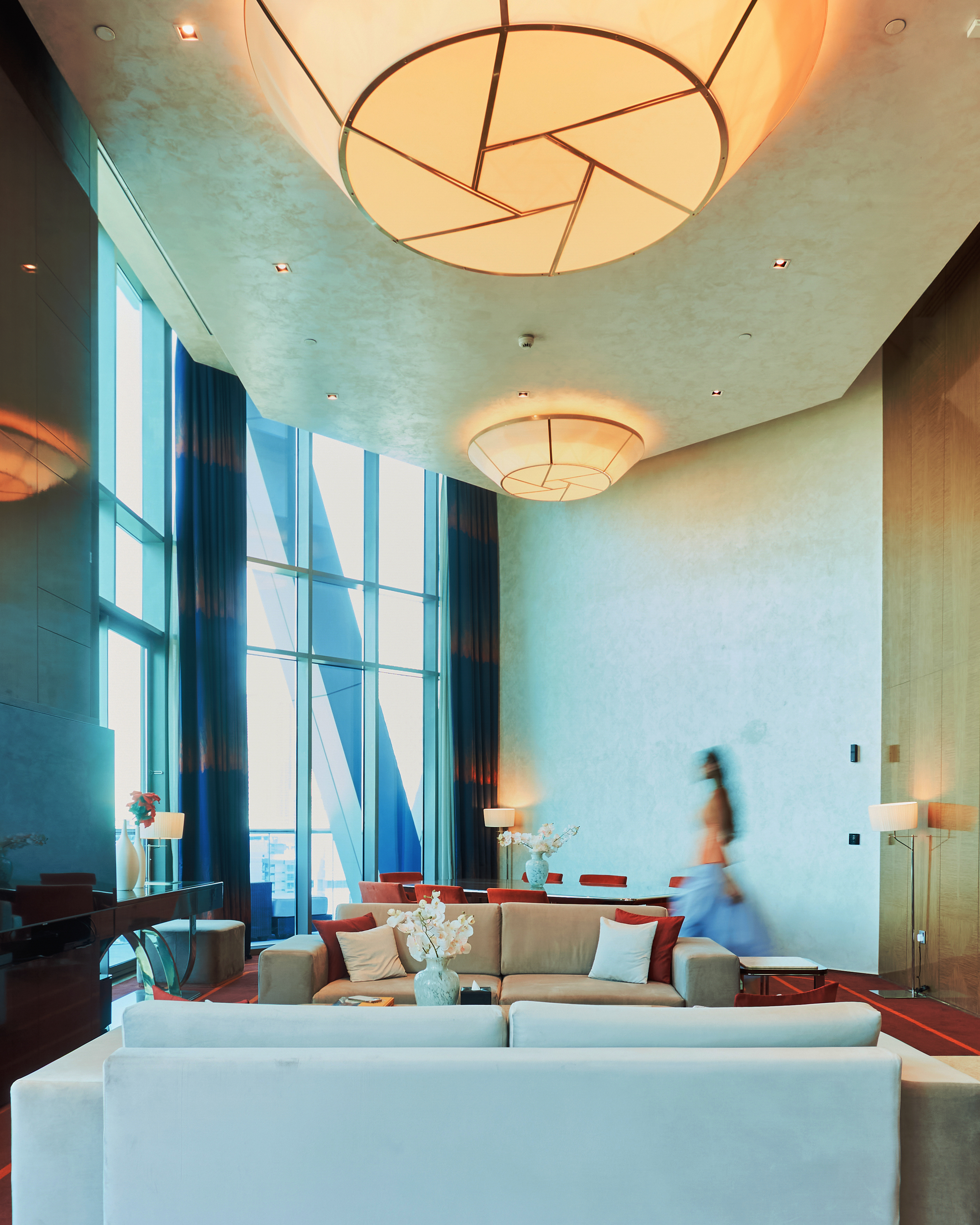 A lady entering the living room of a penthouse with high ceilings, filled with natural daylight.