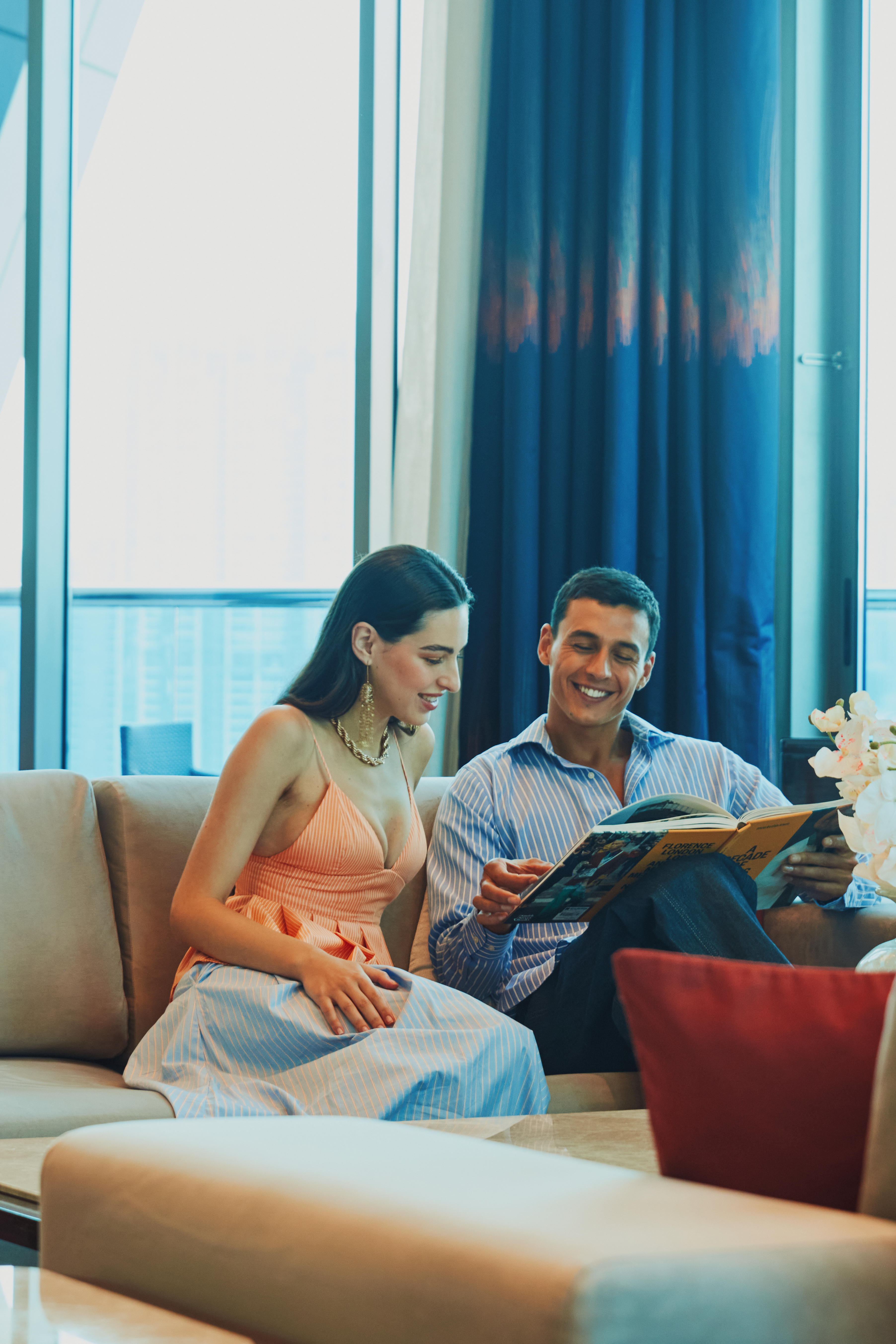 A happy couple, a woman and a man, sitting on a sofa in the living room, reading a book together.