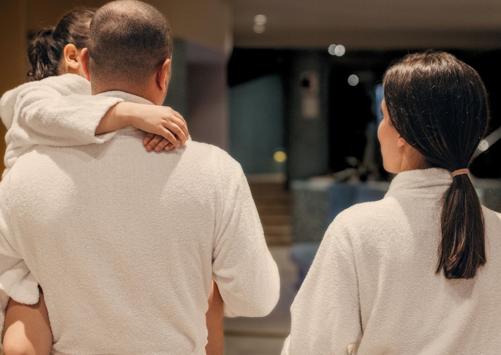 A dad, carrying his daughter, and the mom walking next to them. The family are all in white gowns.