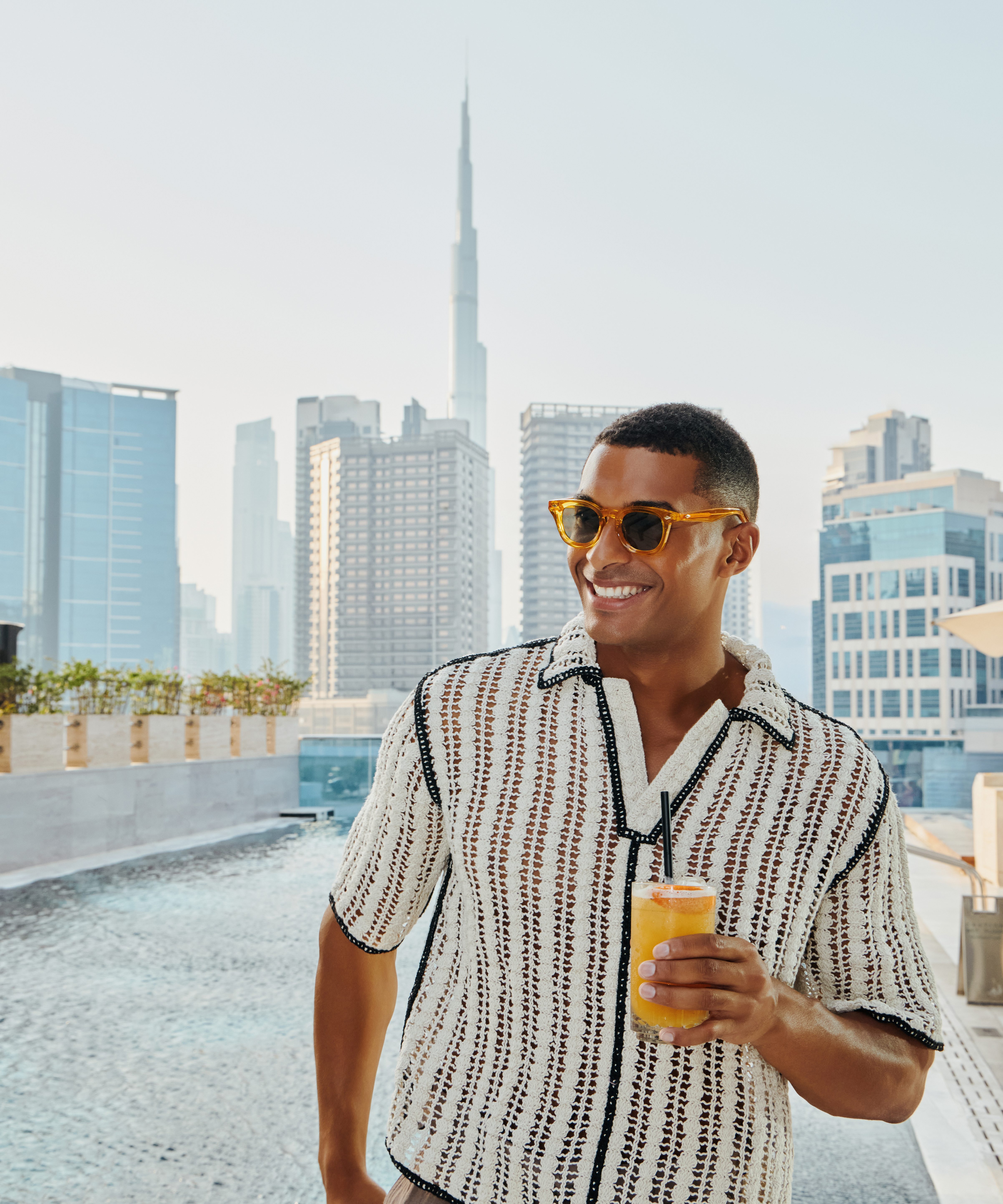 A guy with a drink by the pool with Burj Khalifa Views